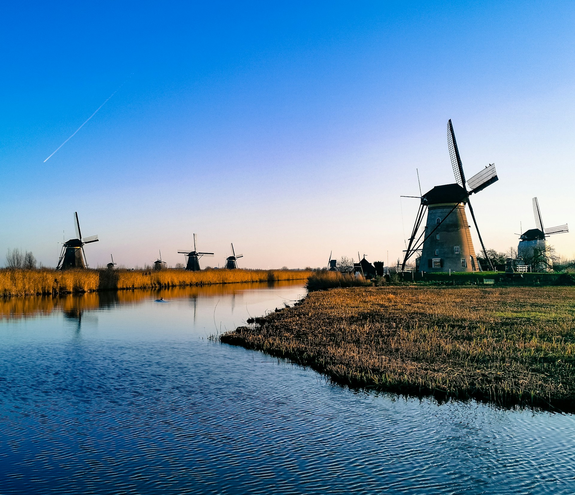 Windmills standing fast at Kinderdijk, with a light breeze across the water in-between giving thought to a nearby past.